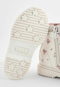 Bottines blanches à imprimé floral, avec fermeture éclair sur le côté et semelle en caoutchouc texturée présentant des accents en forme d'étoile et des lignes nervurées. Taille 36.