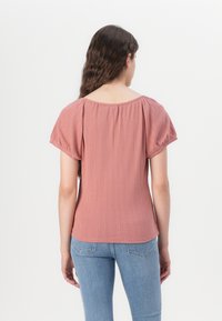 Top roz cu mâneci scurte bufante, design cu dungi texturate și decolteu rotund. Purtați cu blugi ajustați albaștri.