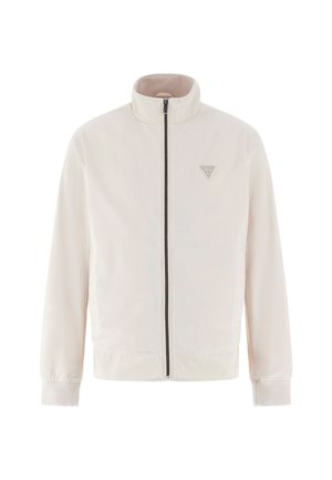 Light beige zip-up jacket with stand collar, long sleeves, ribbed cuffs, and a small triangular logo patch on the chest.