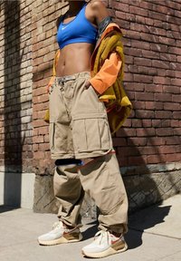 Pantaloni cargo beige con più tasche, abbinati a un reggiseno sportivo blu e a una giacca arancione. Le sneaker presentano dettagli bianchi e arancioni.