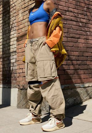 Pantaloni cargo beige con più tasche, abbinati a un reggiseno sportivo blu e a una giacca arancione. Le sneaker presentano dettagli bianchi e arancioni.