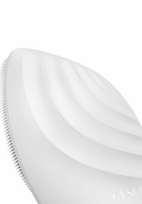 Hvid ansigtsrensningsbørste med et bølget, ergonomisk design. Har bløde silikonebørster og en glat, tekstureret overflade.