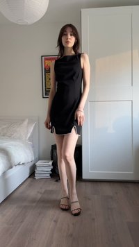 Vestito nero senza maniche con design aderente e spacco laterale decorato con perle bianche. Indossato con tacchi neri con cinturini.