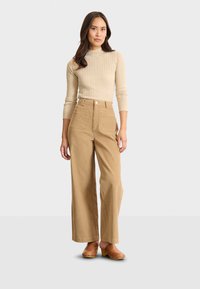 Beige geripptes Strickoberteil, kombiniert mit weit geschnittenen Cord-Hosen in einem hellen Braunton. Die Hosen verfügen über zwei vordere Taschen und eine hohe Taille.