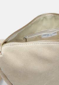 Bežová semišová kabelka na ruku se zlatým zipem, s hladkou podšívkou a malou kapsou na zip označenou "Pravá kůže."