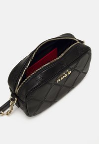Sac à bandoulière en cuir noir avec un motif en relief, matériel doré, fermeture éclair et une poche intérieure rouge. Dispose d'une bandoulière en chaîne.
