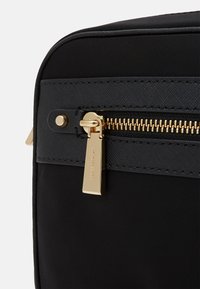 Nahaufnahme einer schwarzen Nylon-Tasche mit goldenen Reißverschluss, rechteckiger Form und glatter Textur, akzentuiert durch einen goldenen Ziehgriff und Nähdetails.
