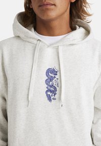 Light gray hoodie with a soft texture. Features a blue dragon graphic on the chest and drawstrings on the hood.