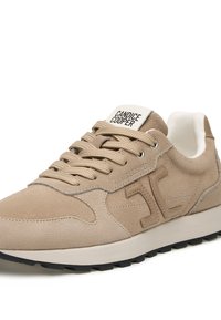 Sneaker in suede beige con lacci spessi, collare bianco imbottito e logo del marchio sul lato e sulla linguetta, su una suola bianca con grip nera.