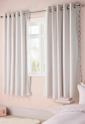Tende a quadretti rosa chiaro e bianco appese a una bacchetta d’argento sopra una finestra in una camera da letto dai colori tenui.