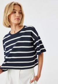 Camiseta de algodón azul marino y blanca a rayas con mangas cortas y escote redondeado, con un corte relajado y textura suave.