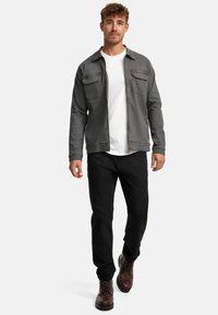 Grå denimjakke med to brystlommer, parret med en hvid t-shirt, sorte bukser og brune læderstøvler. Designet til afslappet brug.