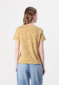 Mustard yellow t-shirt with a floral pattern, short sleeves, and a crew neckline. Material appears soft with a casual fit.