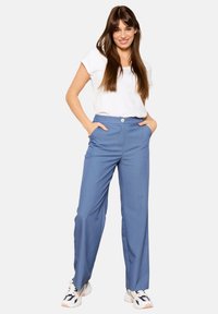 Gaiši zili platās bikses ar gludu tekstūru, ar sānu kabatām un vienu priekšējo pogu. Kombinētas ar baltu t-kreklu.