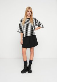 Μακρυμάνικη ριγέ ασπρόμαυρη μπλούζα σε μεγάλο μέγεθος συνδυασμένη με πλισέ μαύρη φούστα. Το μοντέλο φοράει μαύρα αρβυλάκια και ναυτικά πλεκτά καλτσάκια.