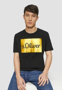 Schwarzes Baumwoll-T-Shirt mit einem goldenen rechteckigen Logo, auf dem "s.Oliver" in schwarzer Schrift steht. Das Design ist schlicht mit kurzen Ärmeln und Rundhalsausschnitt.