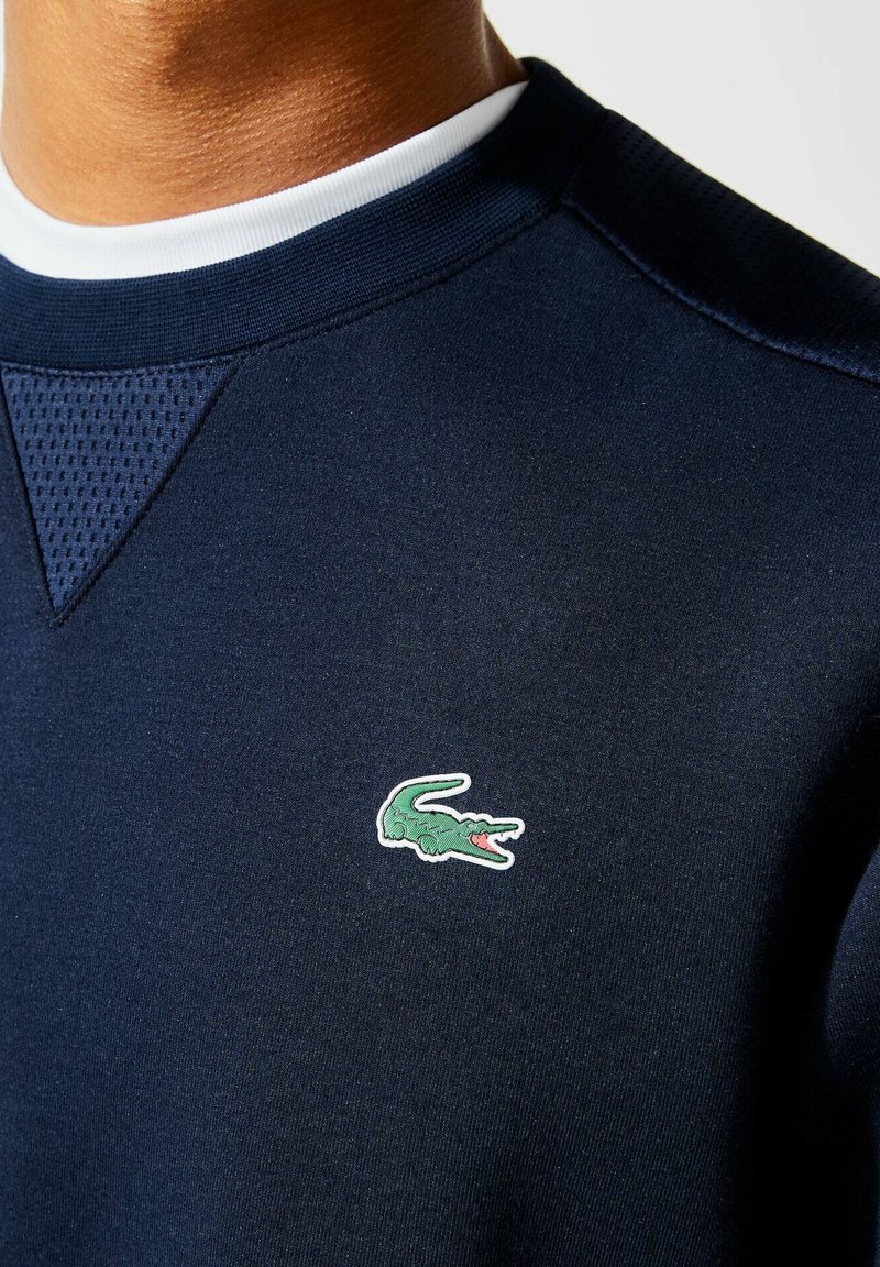 Sweatshirt bleu marine avec un empiècement texturé, un col rond et un petit logo de crocodile vert brodé sur la poitrine.