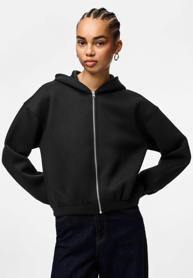Felpa con zip nera, con tasca frontale, vestibilità oversize e orlo a coste. Presenta un cappuccio con coulisse e un tessuto morbido e strutturato.