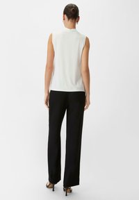 Top bianco senza maniche realizzato in tessuto liscio, abbinato a pantaloni neri larghi. L'outfit presenta una silhouette pulita senza accenti notevoli.