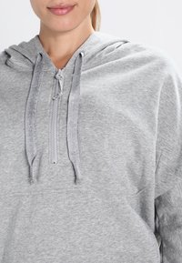 Gray hoodie with a front zipper, drawstring hood, and soft texture. Features a relaxed fit and ribbed accents near the zipper.