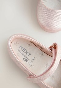 Pink metallic Mary Jane-sko med en tekstureret overdel. Gennemsigtig sål og inderside med sølvbue-mønstre. Fastgjort med en stropp.