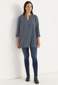 Navy tunic with a geometric white pattern, three-quarter sleeves, a v-neckline, and a loose fit, paired with dark skinny jeans and ankle boots.