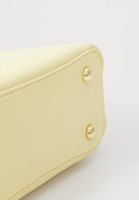 Gul faux lærveske med en glatt tekstur, med gullmetallhardware, nagler og sømmer langs kantene.