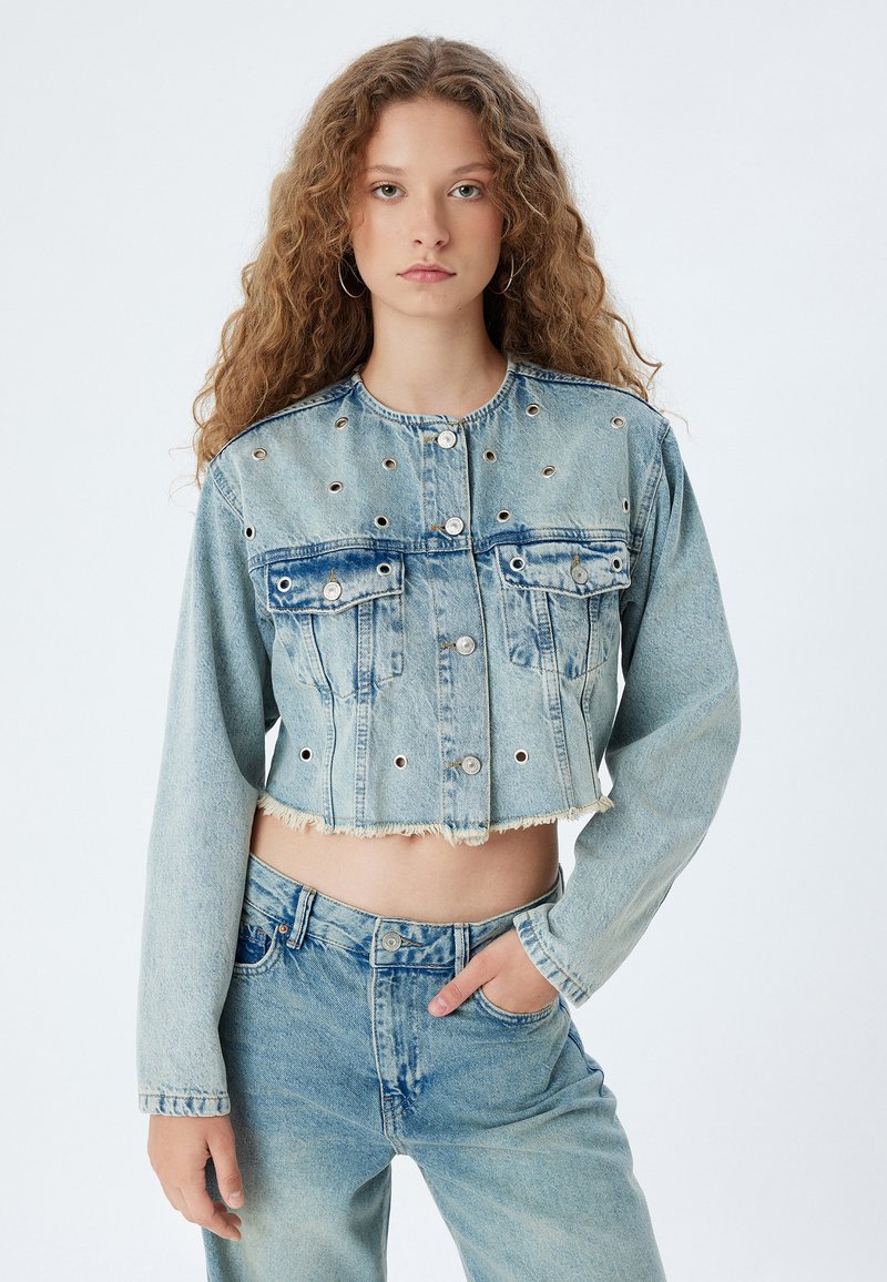 Avkortad blå denimjacka med knappstängning, två framfickor och öljett-detaljer. Fransig fåll och långa ärmar.