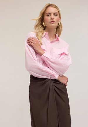 Helles rosa Hemd mit Knopfleiste, zwei Brusttaschen, langen Ärmeln und einer lockeren Passform, kombiniert mit einem dunkelbraunen Rock mit drapierten Details.