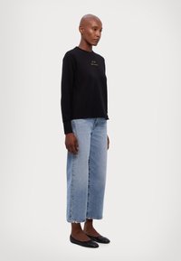 Maglietta nera a maniche lunghe con logo dorato, abbinata a jeans a gamba larga azzurri e ballerine nere, caratterizzata da un design relaxed-fit.