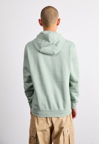 Sweatshirt verde menta com capuz ajustável, punhos e bainha canelados, textura macia, combinado com calças de carga bege, visto de costas.