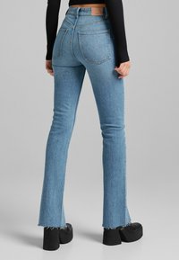 Hellblaue, ausgestellt geschnittene Jeans mit rohem Saum, mittelhoher Taille, klassischem 5-Pocket-Design und subtiler Ausbleichung in der Textur des Stoffes.