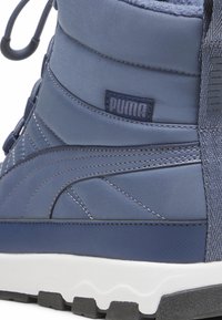 Botín azul de Puma con material sintético texturizado, diseño acolchado, suela blanca y banda de rodadura de goma negra para tracción y durabilidad.