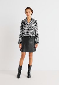 Cropped blazer u crno-bijelom kariranom uzorku, lagani materijal, dvostruki gumbi, uparen s crnom A-line suknjom od umjetne kože i crnim kaubojskim čizmama.