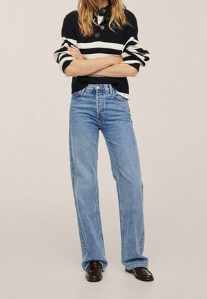 Blauwe jeans met hoge taille en een rechte pijp, licht gewassen en met weinig slijtage, gecombineerd met een zwart-wit gestreepte trui.