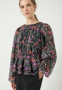 Svart blomstrete peplumtopp med puffede ermer, med flerfargede blomsterpatroner, semigjennomsiktig stoff og detaljert rynket halslinning.