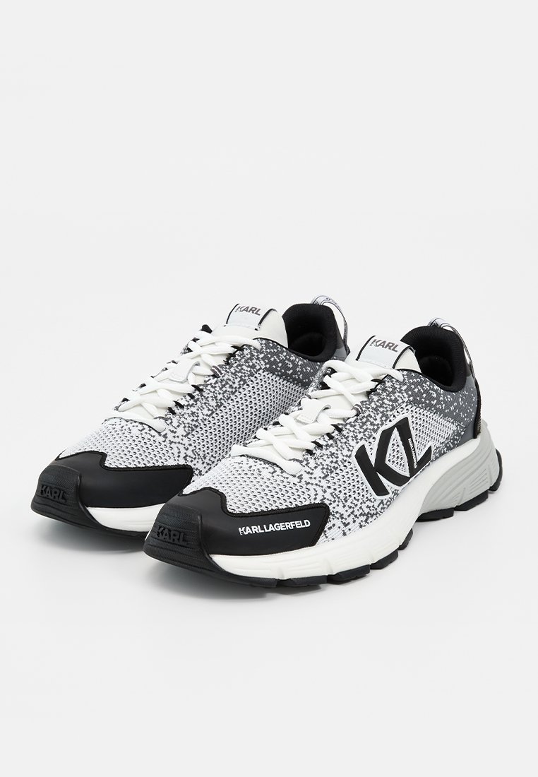 Zapatillas blancas y negras Karl Lagerfeld con textura tejida, cierre de cordones y marca en el lateral, la lengüeta y la puntera, mostradas desde un ángulo frontal.