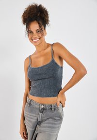 Šedý žebrovaný crop top s tenkými ramínky, který je zkombinován se šedými džíny s vysokým pasem a jemným odbarvením.