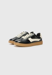 Black and cream sneakers with a smooth leather upper, chunky gum rubber sole, and lace-up design, featuring a white accent on the side.
