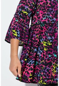 Bunte, gemusterte Bluse mit kurzen Glockenärmeln. Der Stoff zeigt abstrakte Flecken in Schwarz, Pink, Lila und Grün. Ausgestellt, lockere Passform.