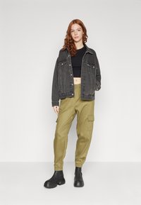 Svart denimjacka, kort svart topp, olivgrön cargobyxa med sidofickor och svarta ankle boots. Släta texturer och avslappnad passform.