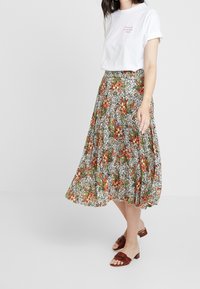 Blommig midi kjol med vit bakgrund och orange och gröna mönster, i kombination med en enkel vit t-shirt och bruna slidesandaler.