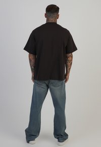 Sort bomulds T-shirt med korte ærmer og lige snit, parret med lyseblå løse denimjeans og hvide sneakers.