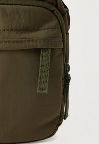 Κοντινή λήψη χλιαρής ελιάς υφασμάτινου πουγκιού με φερμουάρ και ραμμένη ταινία τράβηγμα σε ανοιχτό φόντο.