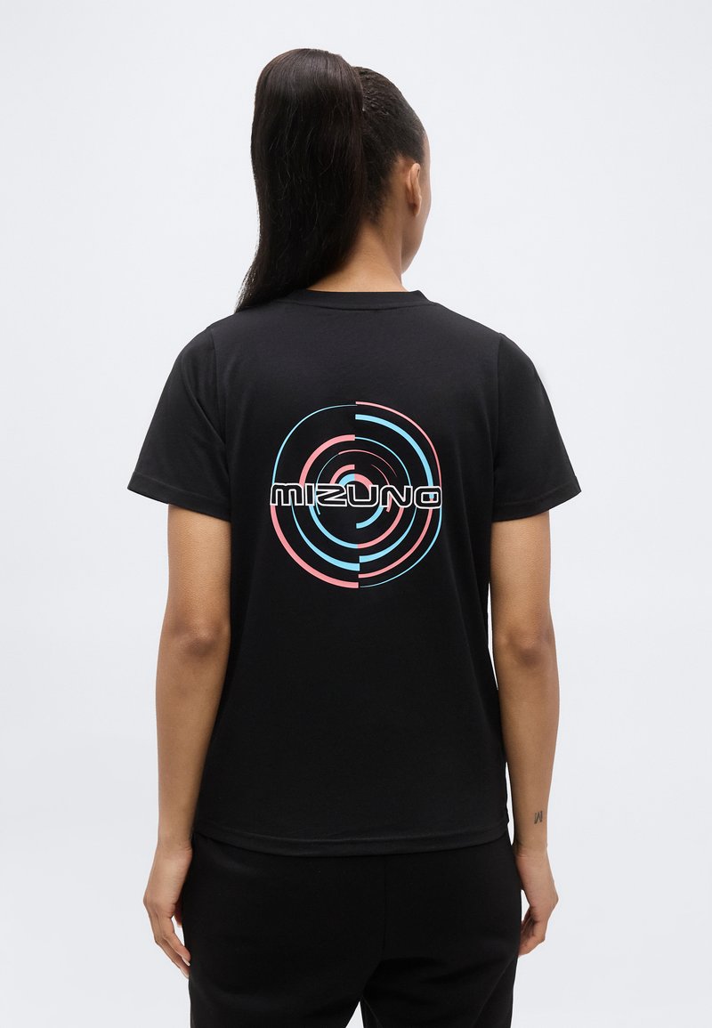 Άτομο με μακριά σκούρα μαλλιά σε αλογοουρά, φοράει μαύρο T-shirt με πολύχρωμο κυκλικό λογότυπο "Mizuno" στην πλάτη.