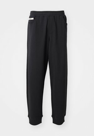 Pantalons de survêtement noirs en tissu doux, avec une taille élastique, des poches latérales et des poignets côtelés aux chevilles. Design minimaliste.