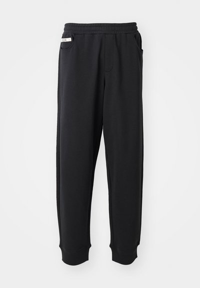 Black sweatpants made of soft fabric, featuring an elastic waistband, side pockets, and ribbed cuffs at the ankles. Minimalist design.