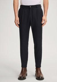 Granatowe, dopasowane spodnie z płaskim przodem, z bocznymi kieszeniami i pojedynczym zapięciem na guzik, wykonane z gładkiego, teksturowanego materiału, w połączeniu z brązowymi butami.
