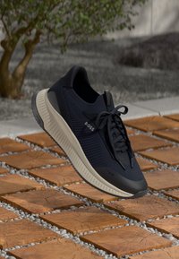 Dark blue athletic sneaker with mesh and rubber materials, featuring a textured upper, flat laces, and a light-colored sole.