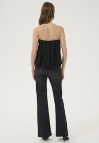 Schwarzes, trägerloses Oberteil mit plissiertem Design; kombiniert mit hoch taillierten schwarzen Schlagjeans. Glatte Textur ohne sichtbare Muster.